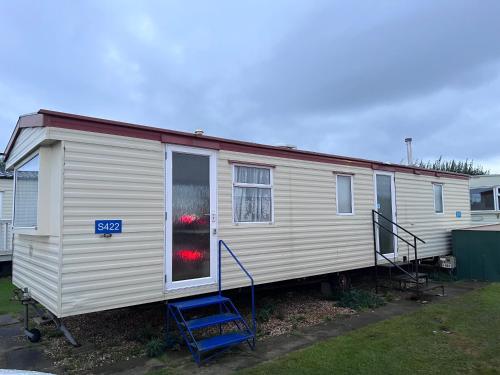 a white mobile home with a blue staircase and a house at S422 Golden Palm 8 Berth Caravan in Chapel Saint Leonards