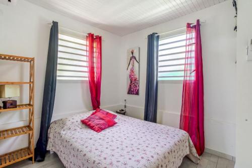 a bedroom with a bed with red pillows and windows at Ti-colibri ✓Iguana Village in Sainte-Luce