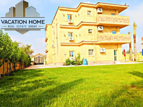 a yellow house on a green lawn in front of a building at الريف الاوروبي in 6th Of October