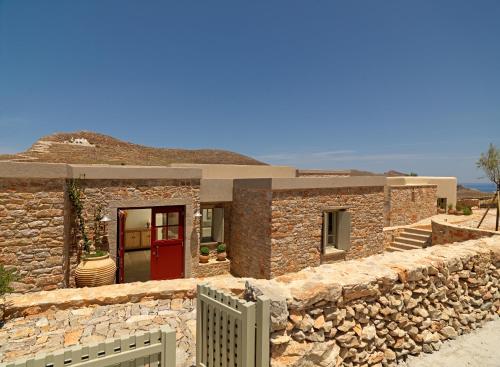 a stone house with a red door and a stone wall at Themonies Luxury Suites in Chora Folegandros