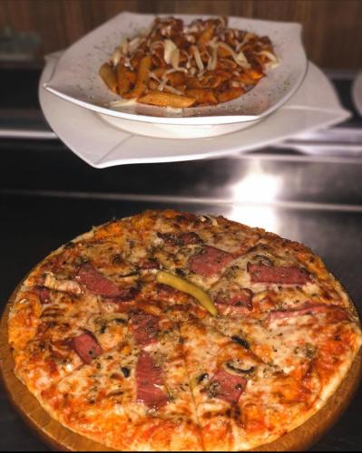 a pizza on a plate and a plate of pasta at Hotel sofra in Ferizaj