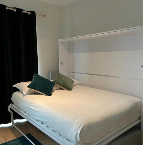 ein weißes Bett mit zwei grünen Kissen darauf in der Unterkunft Central fully serviced studio in Luxemburg (Stadt)