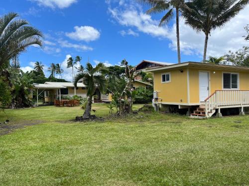 a yellow house with palm trees in front of a yard at Aaron’s cottage in Hilo
