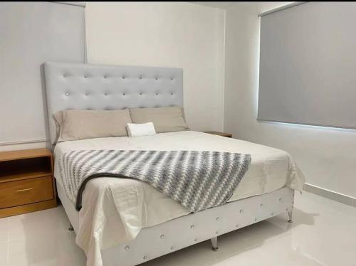 ein Schlafzimmer mit einem weißen Bett mit einer grauen und weißen Decke in der Unterkunft Hermoso apto 804 en Villa María in Santiago de los Caballeros