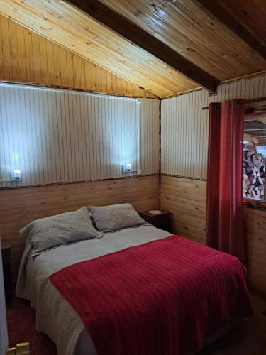 - une chambre avec un lit et une couverture rouge dans l'établissement Cabañas Robinson, à Puerto Puyuhuapi