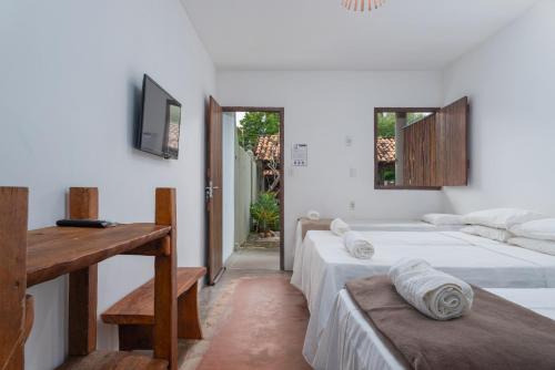 a bedroom with two beds and a table and a television at Pousada Trilha do Mar in Praia do Frances