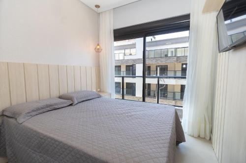 a bedroom with a bed and a large window at 139C - lindo apartamento a 50m da praia de Canto Grande in Bombas