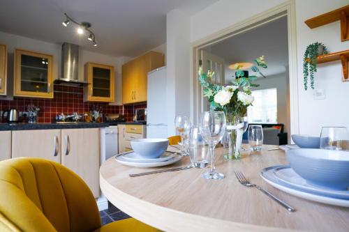 a kitchen with a wooden table with plates and wine glasses at Stunning Harvest Way House in Witney