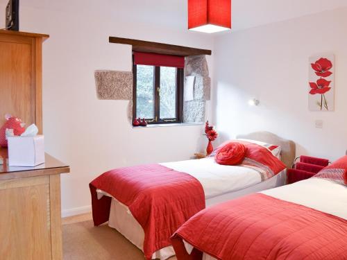 a bedroom with two beds with red sheets and a window at Little Content Farm Cottage in Cury