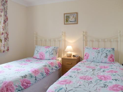 - 2 lits dans une chambre ornée de fleurs roses dans l'établissement Carols Cottage - E3043, à Blyford