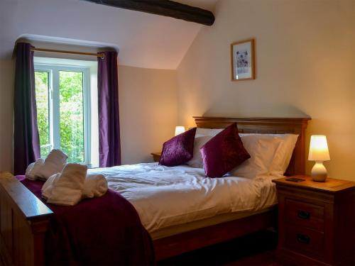 a bedroom with a bed with purple pillows and a window at Tyddyn Eli in Llangwm