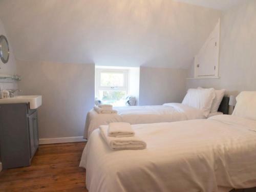 two beds in a room with white sheets and a sink at Little Trevarrack in Carbis Bay