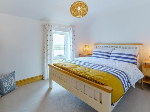 a bedroom with a bed with a yellow blanket and a window at Tyr Llyr in Penclawdd