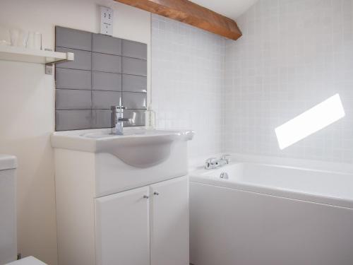 a white bathroom with a sink and a bath tub at Barn Cottage in Talley