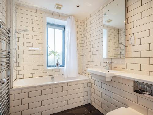a white tiled bathroom with a sink and a window at Killantrae Burn in Port William
