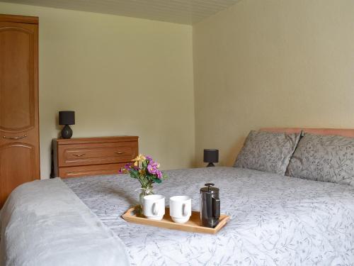 a bed with two mugs and flowers on a tray at Ben View in Orbliston