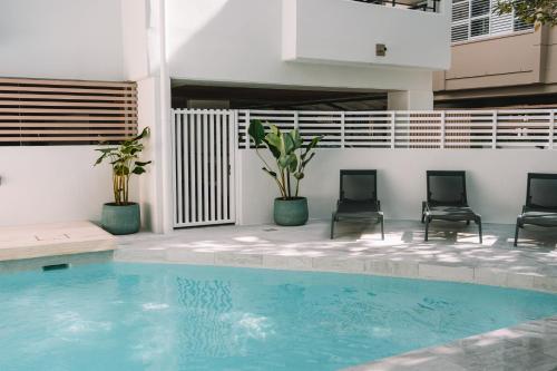 a swimming pool with two chairs and a building at Bella Casa Noosa in Noosa Heads