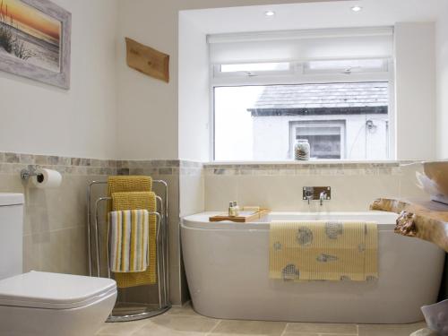 a bathroom with a tub and a toilet and a window at Rhunahaorine Cottage in Gortinanane