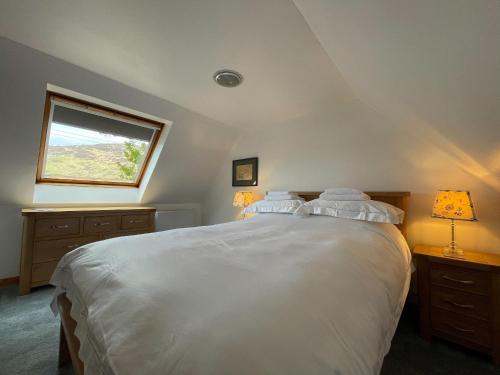 a bedroom with a large white bed with a window at Lag Cottage in Dornie