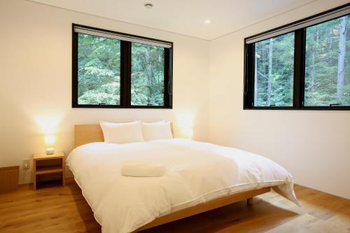 a bedroom with a large white bed with two windows at SEVEN TREES BY AOKIKO in Omachi