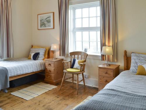 a bedroom with two beds and a chair and a window at Lighthouse Cottage in Happisburgh