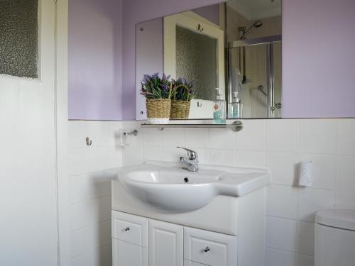 a white bathroom with a sink and a mirror at Brae Cottage in Kelton