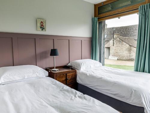 two beds in a bedroom with a window and a table at The Barn At Daubeneys in Colerne