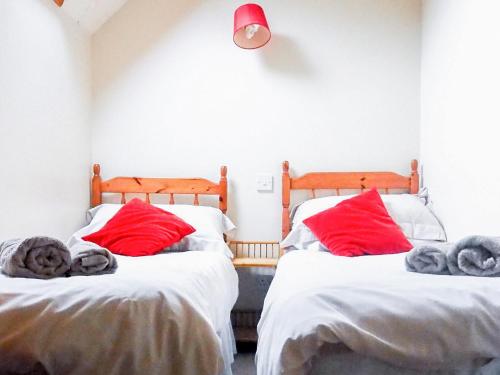 two beds in a room with red pillows at May Cottage in Hackness