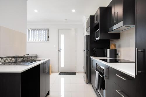 une cuisine avec des armoires noires et des comptoirs blancs dans l'établissement Modern & Beautifully Presented! Close to Transport, à Brisbane