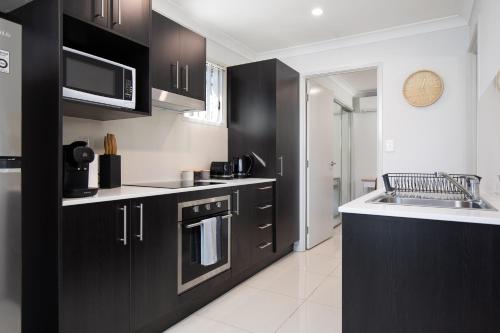 a kitchen with black cabinets and a sink at Modern & Beautifully Presented! Close to Transport in Brisbane