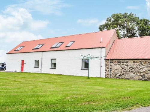 a white building with a red roof and a grass field at The Byre - Uk33397 in Isle of Gigha