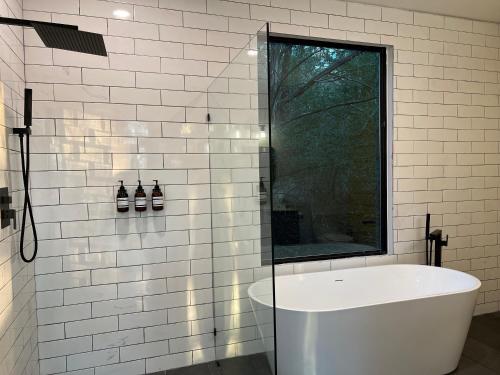 La salle de bains est pourvue de carrelage blanc, d'une baignoire et d'une fenêtre. dans l'établissement Relaxing Modern stay on a Ranch, à Cedar Creek
