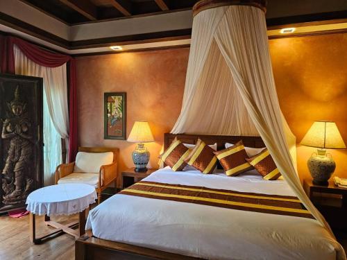 a bedroom with a canopy bed and a chair at Amata Lanna Village อมตะล้านนาวิลเลจ in Chiang Mai