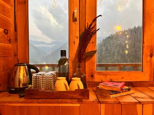 a table with a window with a view of a mountain at Nebula Nook Cottages in Jibhi