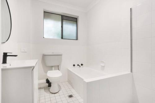 a white bathroom with a toilet and a sink and a shower at Central Cronulla Apartment Nestled in the Treetops in Cronulla