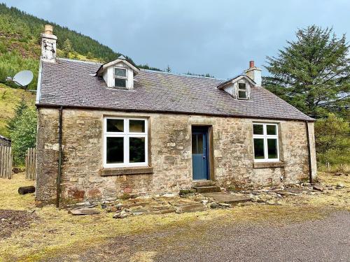 uma pequena casa de pedra com uma porta azul em Glen Hurich Cottage em Scotstown