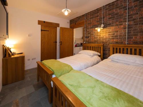 a bedroom with two beds and a brick wall at Cart Shed in Mauchline