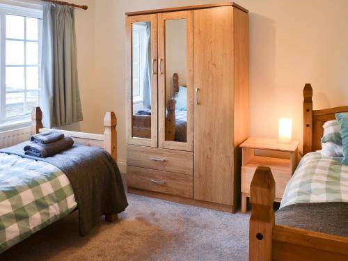 a bedroom with two beds and a large wooden cabinet at Bramble Cottage in Craster