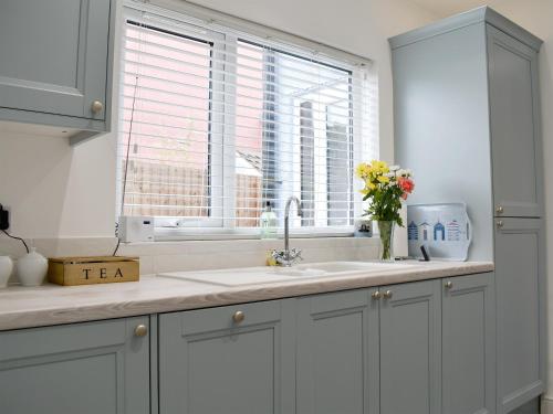 a white kitchen with a sink and a window at Sapphire Cottage in Pakefield
