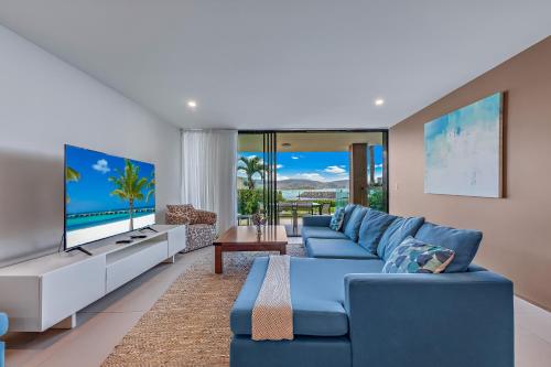 sala de estar con sofá azul y TV en Mirage Whitsundays, en Airlie Beach