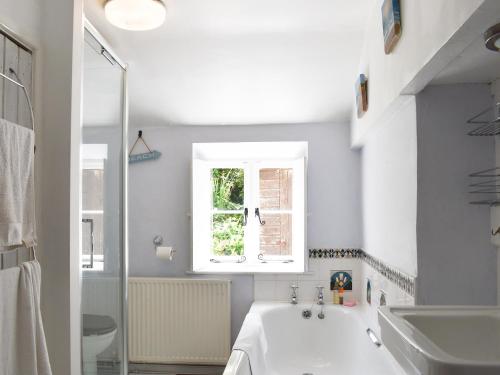 een witte badkamer met een bad en een raam bij Flood House in Bridport