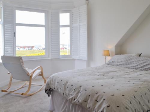a white bedroom with a bed and a chair at Helena in Prestwick
