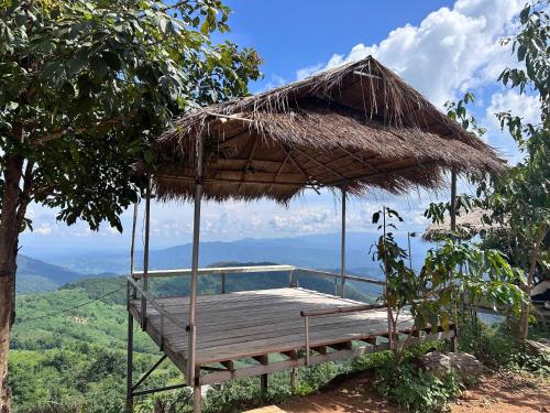 een houten terras met een rieten paraplu op een heuvel bij อาข่าภูมา-Akha Phuma 