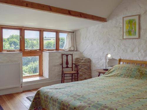 a bedroom with a bed and a chair and windows at Lordship Farmhouse in Saint Lawrence