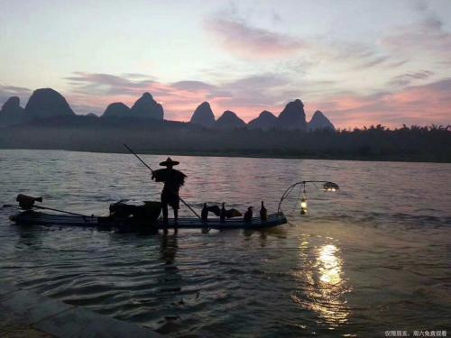 a man is fishing on a boat in the water at Yangshuo Sugar House in Yangshuo