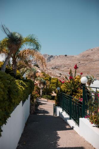 a walkway with palm trees and a fence at Lambis Studios & Apartments in Líndos