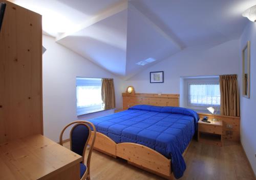 Un dormitorio con una cama azul y una mesa en Hotel Stella Alpina, en Fai della Paganella