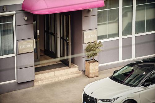 ウィーンにあるHotel Calmoのピンクの日よけ付きの建物の外に停めた車