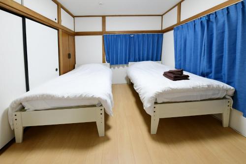 2 łóżka w małym pokoju z niebieskimi zasłonami w obiekcie JH Yellow Guest House w Tokio