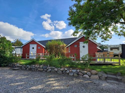 a red and white barn with a tree and rocks at Hytte - 1 rums hytter in Vig